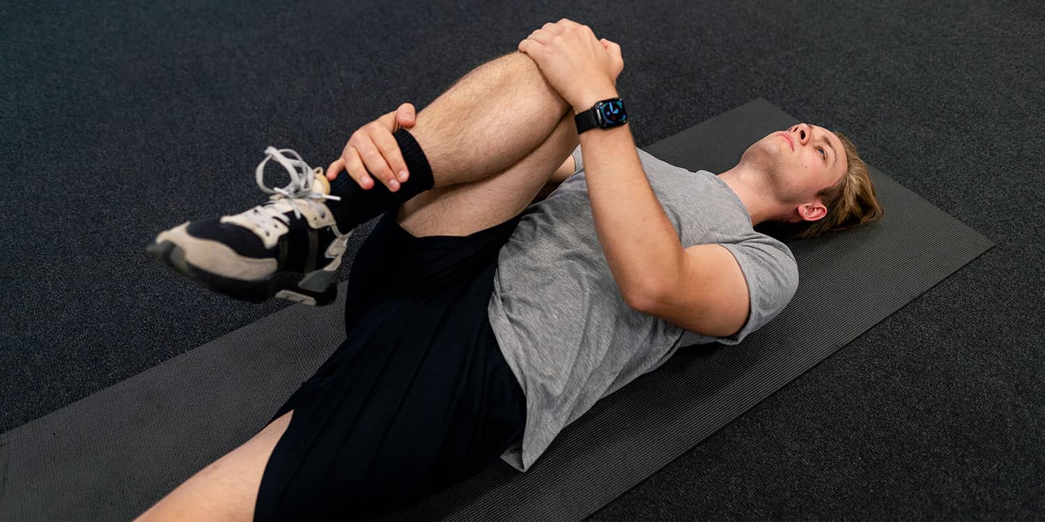 Person doing a lying knee-to-chest stretch on an exercise mat for at-home stress relief and lower-body tension release.