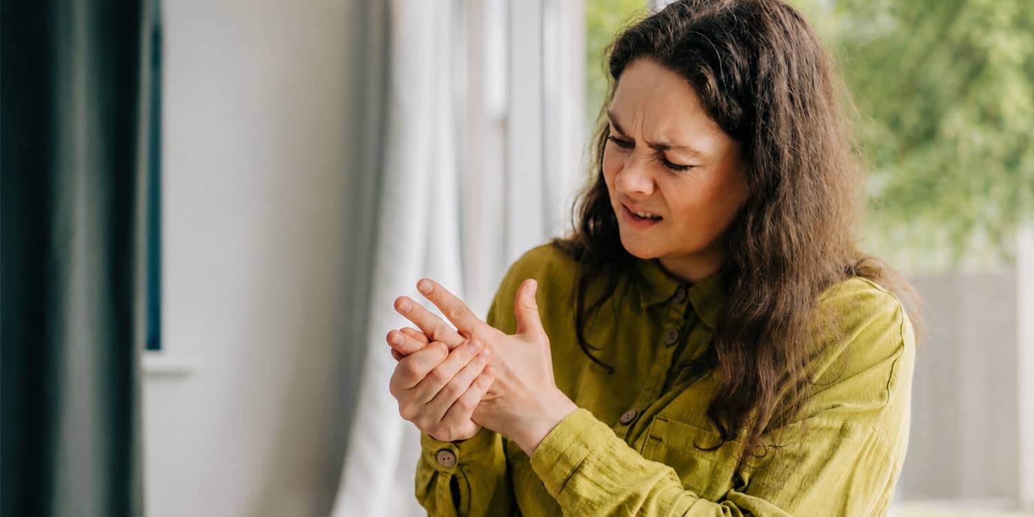 Woman holding a painful hand after a jammed finger, showing discomfort from a jammed joint.