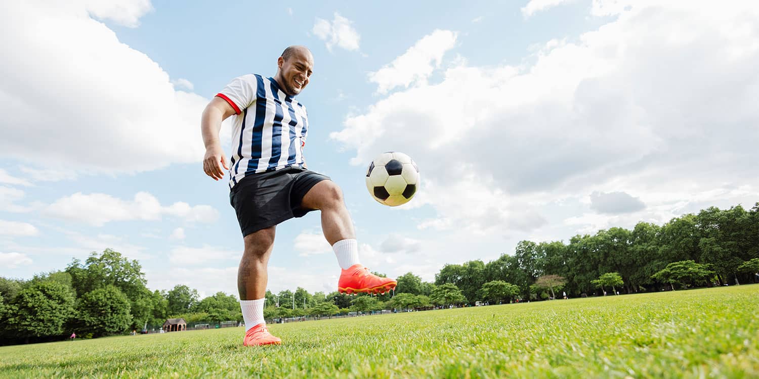 Adult soccer player improving soccer performance, mobility, and recovery with ball control practice on a grass field